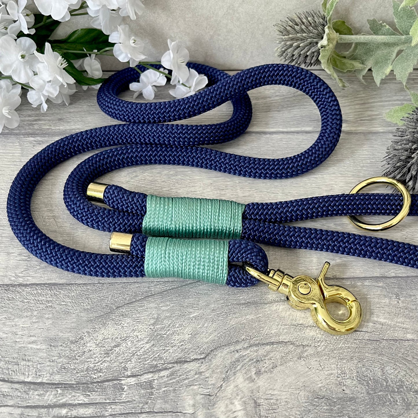 Marine Blue rope lead with Sea Green whipping securing a swivel clip at one end and fastening a handle at the other. The handle has an O-ring attached. Each end of the rope is finished with a metal end cap. All hardware for this lead is in Gold