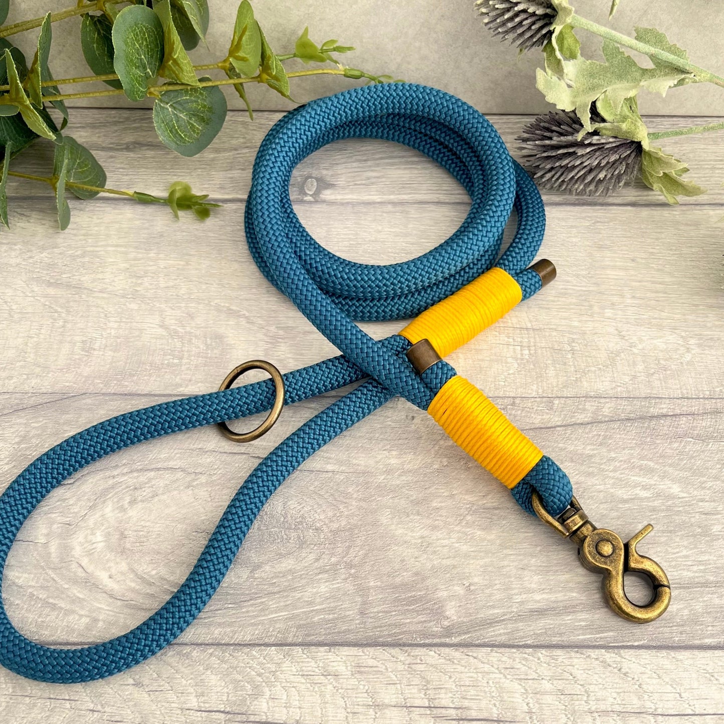 Petrol Blue rope lead with Honey whipping securing a swivel clip at one end and fastening a handle at the other. The handle has an O-ring attached. Each end of the rope is finished with a metal end cap. All hardware for this lead is in Antique Brass