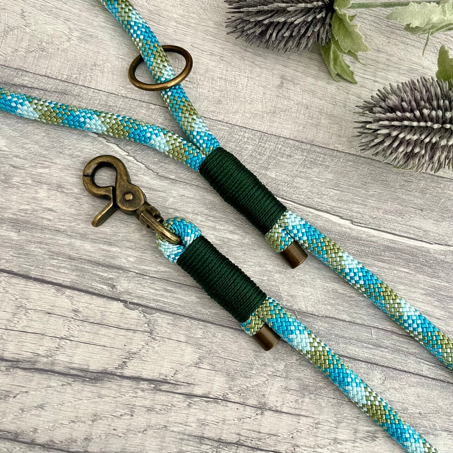 Bombay Blue Paracord rope lead with Dark Green whipping securing each end together. At each end of the rope there is a metal end cap, a clip to connect to a collar at one end and a O-ring fixed to the handle. All hardware Antique Brass
