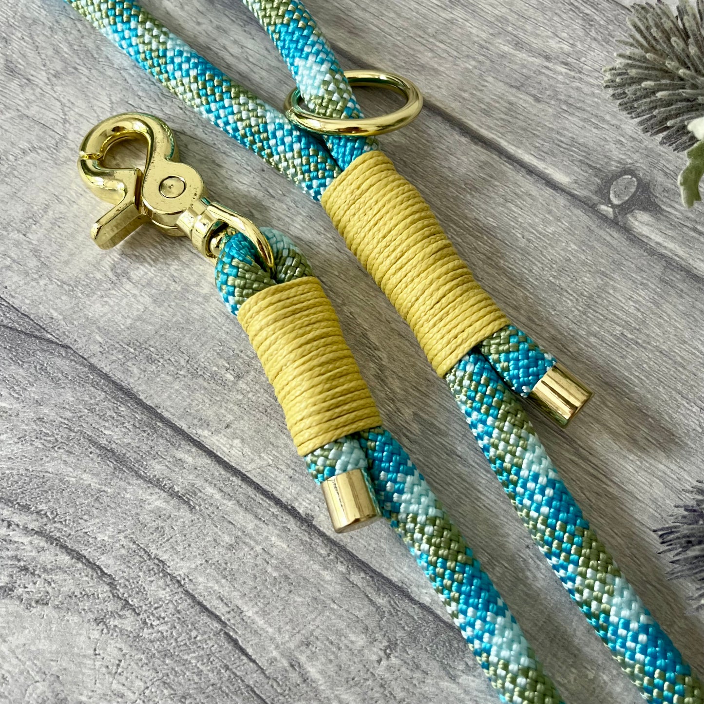 Bombay Blue rope lead with Pastel Yellow whipping securing a swivel clip at one end and fastening a handle at the other. The handle has an O-ring attached. Each end of the rope is finished with a metal end cap. All hardware for this lead is in Gold