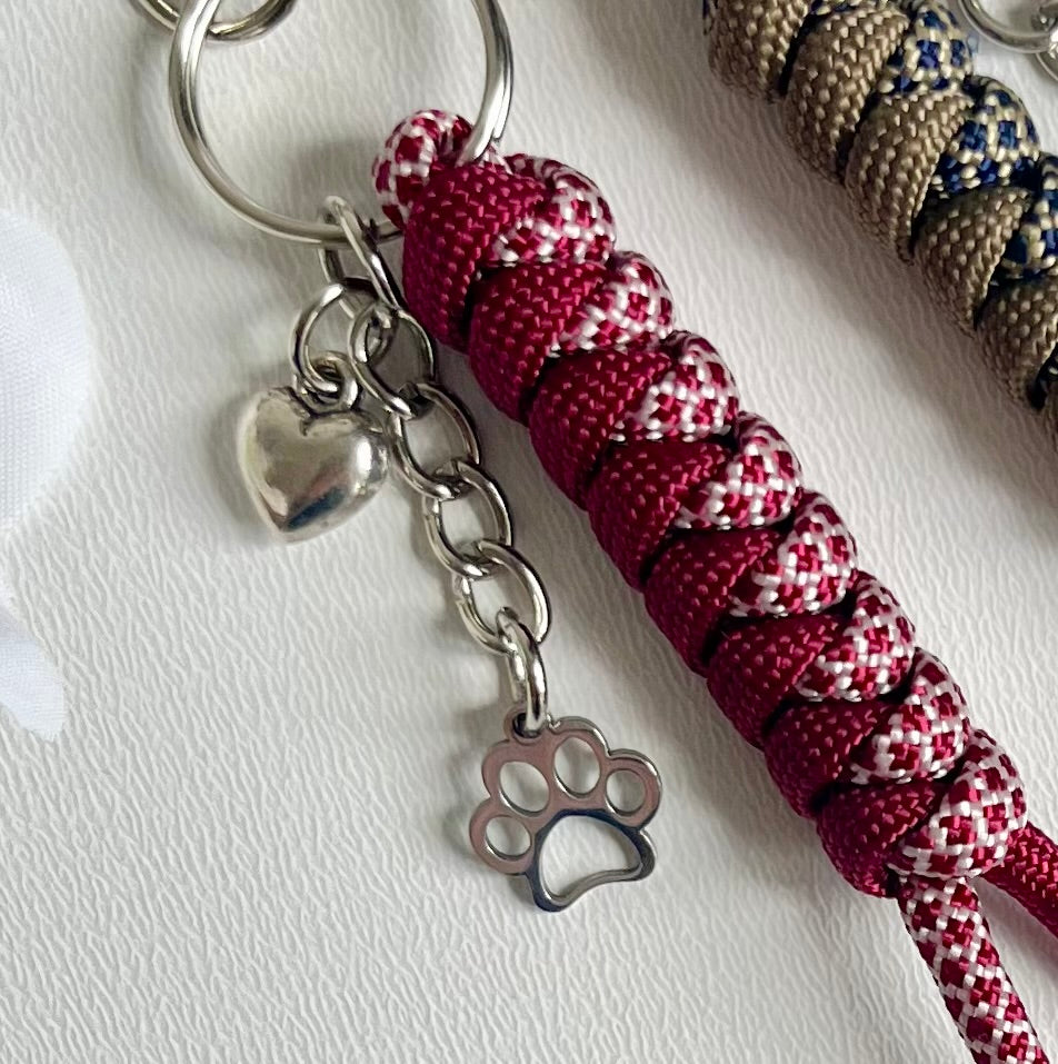 Paracord Keychain with red and white patterned cord, metal heart charm, and paw print charm on a white background.