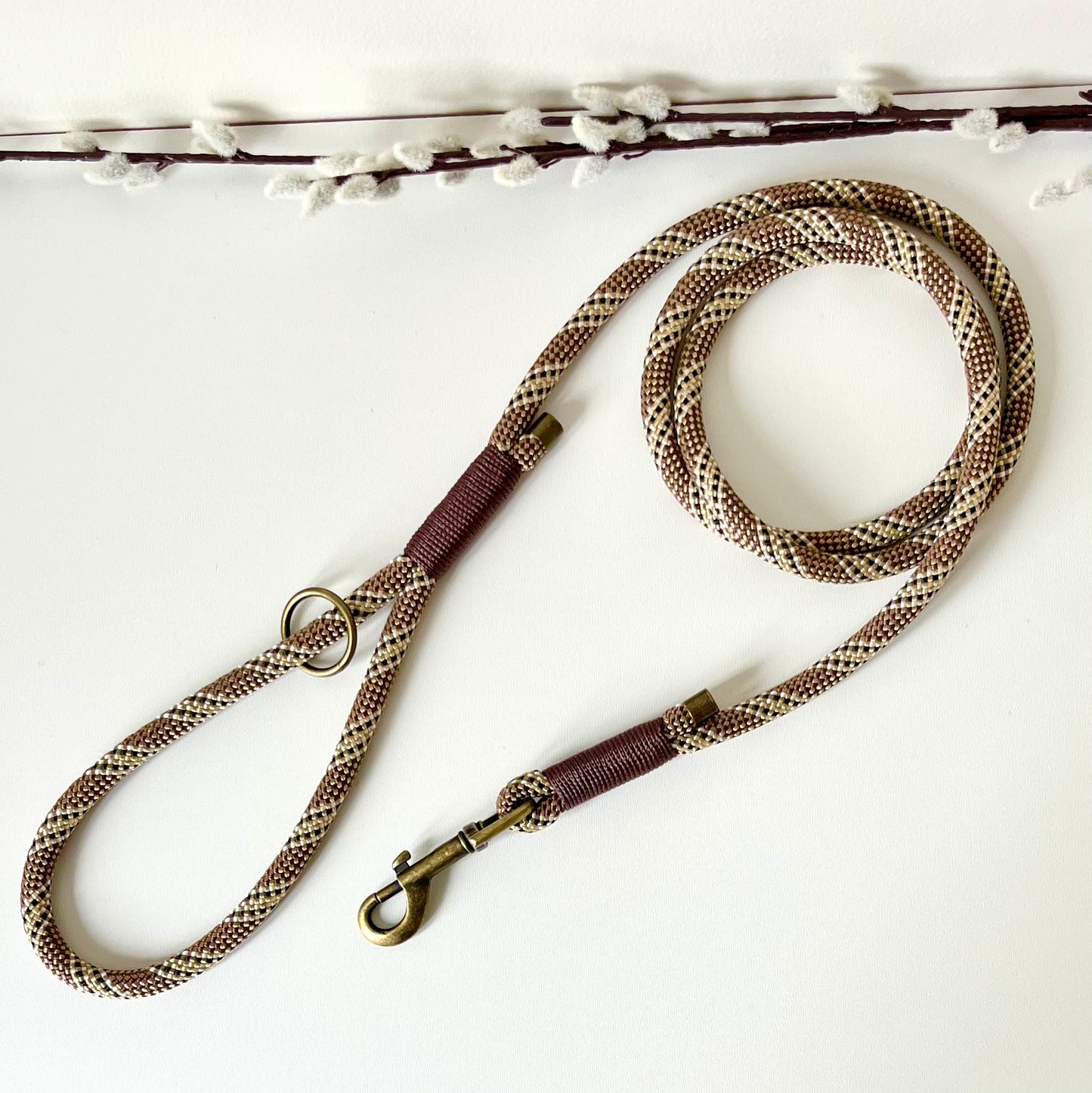 Brown rope dog lead with binding and antique brass hardware on a white surface