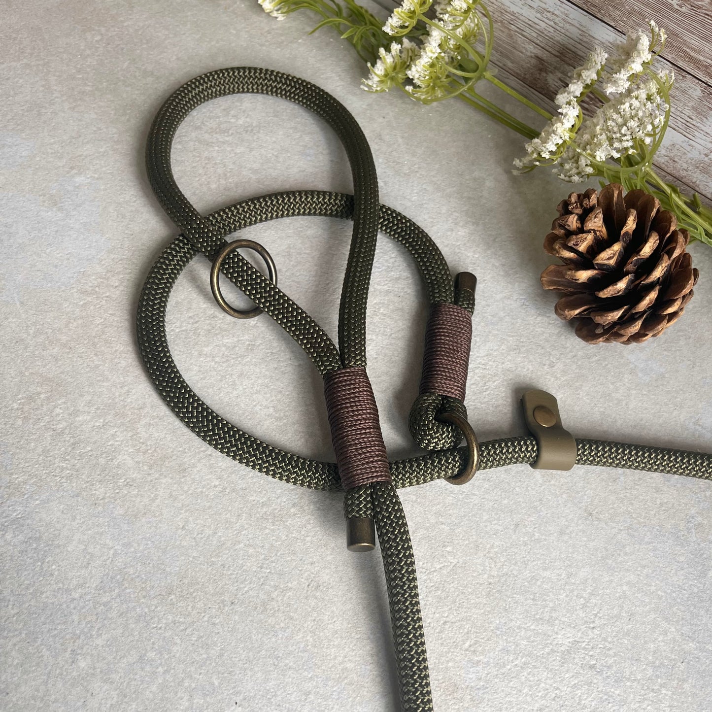 Olive Green Paracord rope slip lead with Brown whipping securing each end together. At each end of the rope there is a metal end cap with a Biothane stopper and a O-ring fixed to the handle. All hardware is Antique Brass