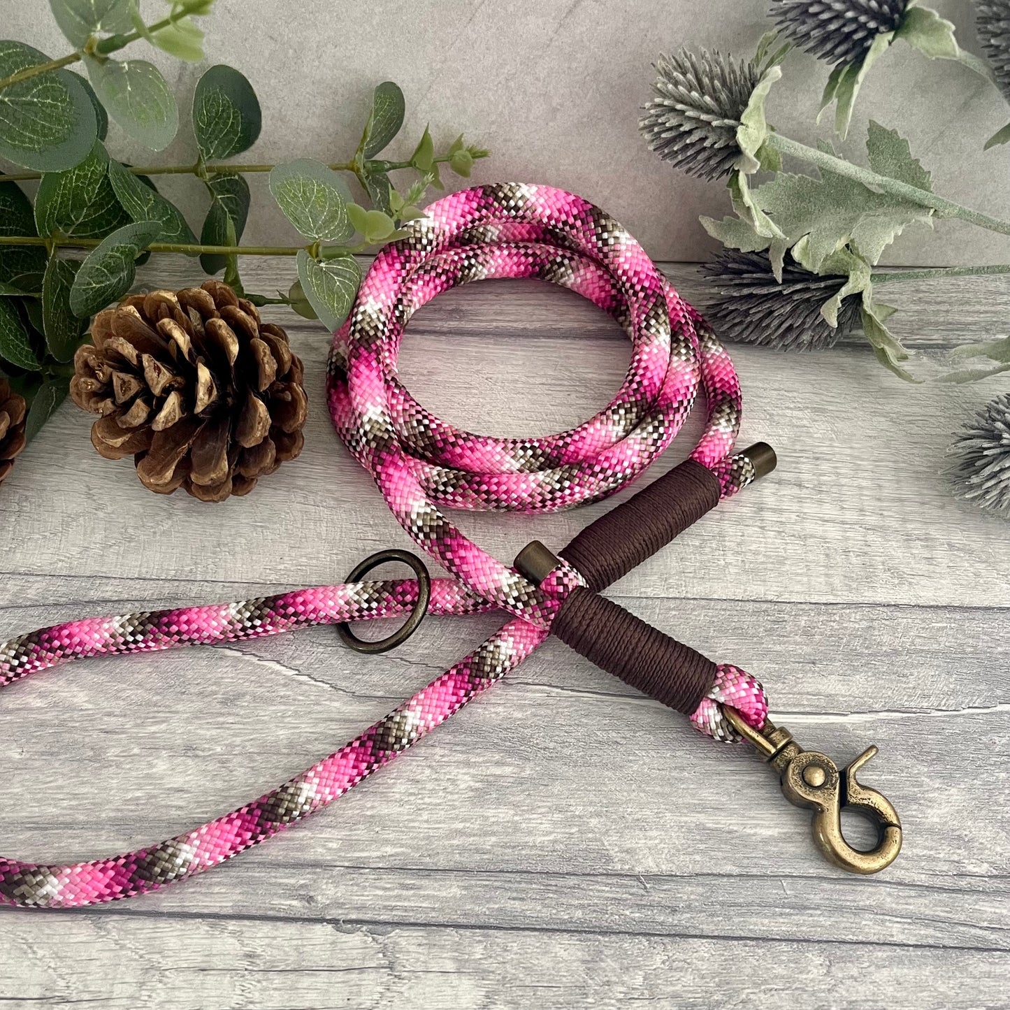 Cowgirl, pink mix Paracord rope lead with Brown whipping securing each end together. At each end of the rope there is a metal end cap, a clip to connect to a collar at one end and a O-ring fixed to the handle. All hardware is Antique Brass