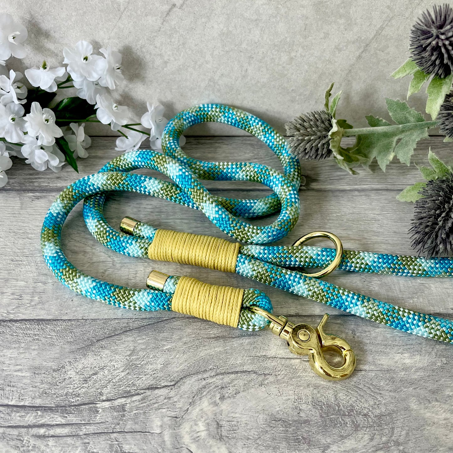Bombay Blue rope lead with Pastel Yellow whipping securing a swivel clip at one end and fastening a handle at the other. The handle has an O-ring attached. Each end of the rope is finished with a metal end cap. All hardware for this lead is in Gold