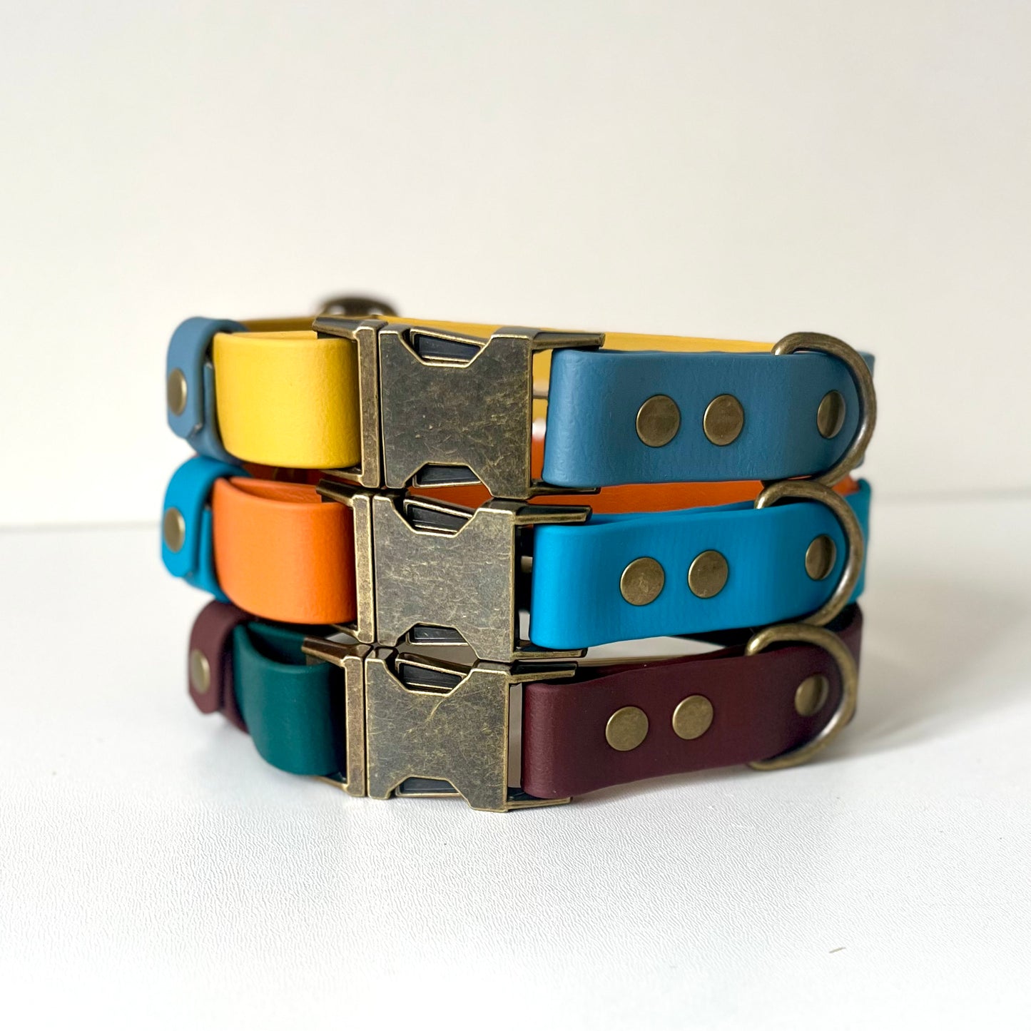 A stack of dog collars in various colours with antique brass hardware
