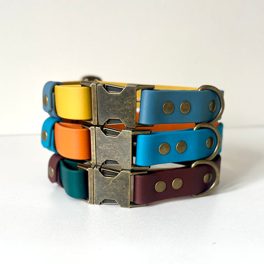 A stack of dog collars in various colours with antique brass hardware