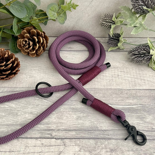 Mauve Paracord rope lead with Aubergine whipping securing each end together. At each end of the rope there is a metal end cap, a clip to connect to a collar at one end and a O-ring fixed to the handle. All hardware is Black