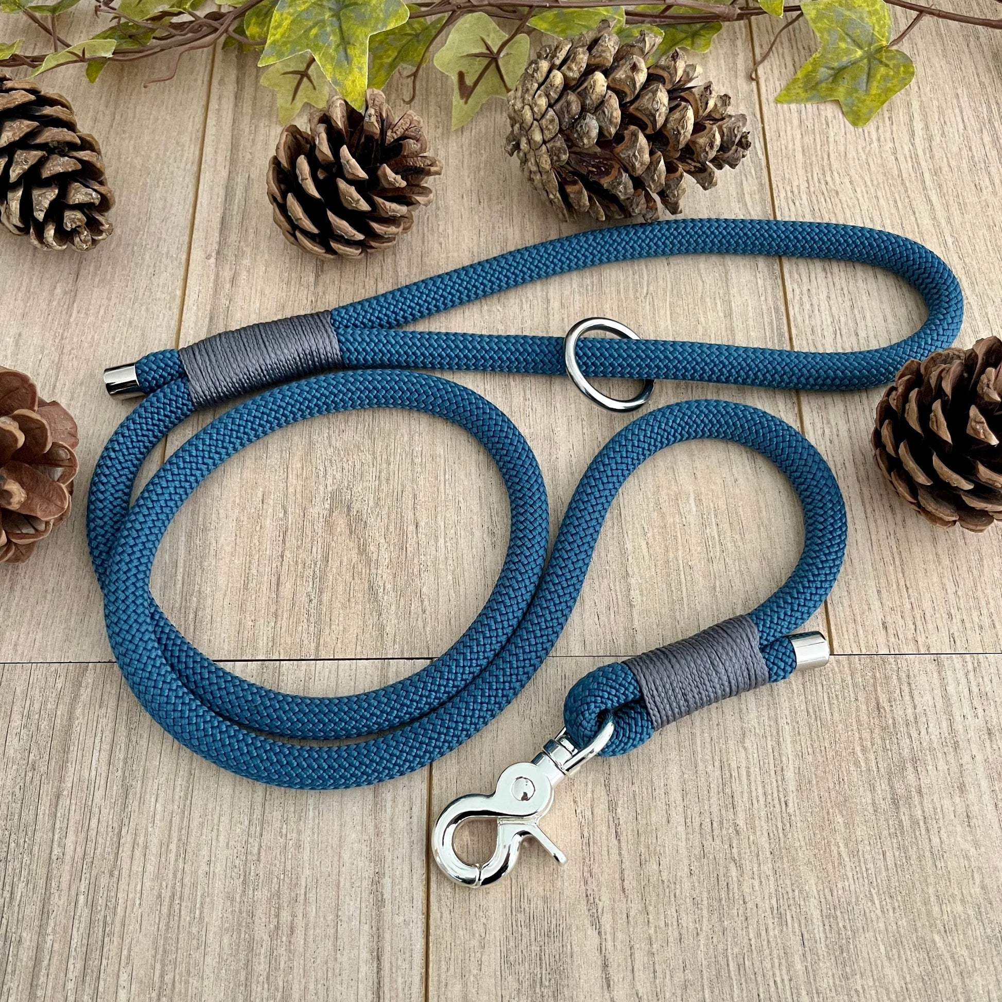 Petrol Blue rope lead with Charcoal whipping securing a swivel clip at one end and fastening a handle at the other. The handle has an O-ring attached. Each end of the rope is finished with a metal end cap. All hardware for this lead is in Sliver