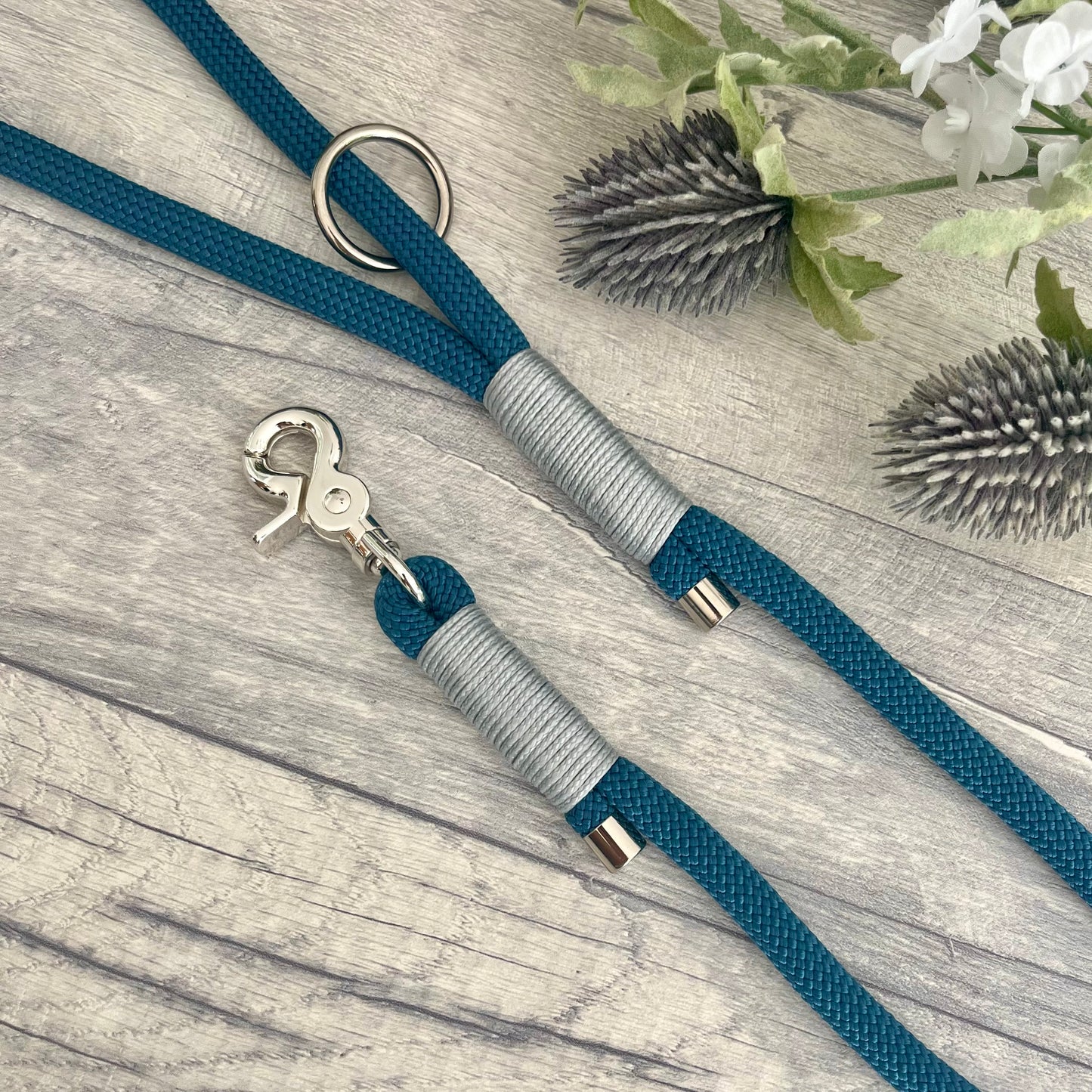 Petrol Blue rope lead with Silver Grey whipping securing a swivel clip at one end and fastening a handle at the other. The handle has an O-ring attached. Each end of the rope is finished with a metal end cap. All hardware for this lead is in Sliver