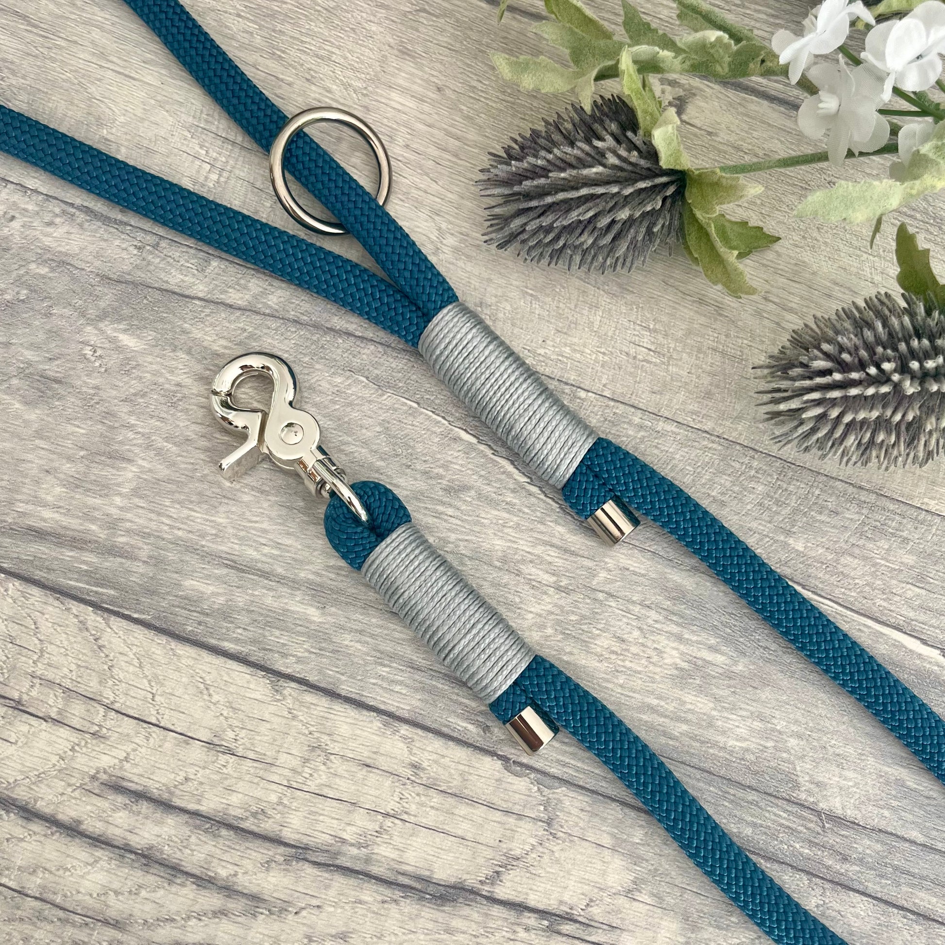 Petrol Blue rope lead with Silver Grey whipping securing a swivel clip at one end and fastening a handle at the other. The handle has an O-ring attached. Each end of the rope is finished with a metal end cap. All hardware for this lead is in Sliver