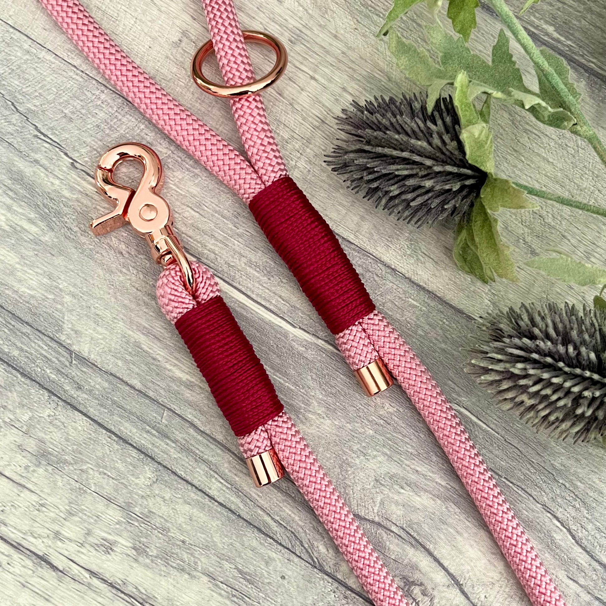 Pink rope lead with Raspberry whipping securing a swivel clip at one end and fastening a handle at the other. The handle has an O-ring attached. Each end of the rope is finished with a metal end cap. All hardware for this lead is in Rose Gold