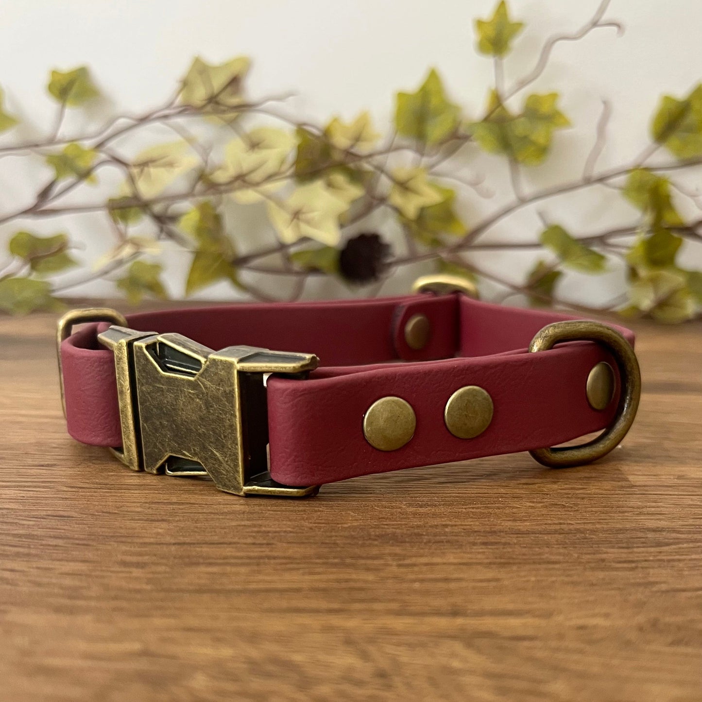 Made from Biothane in Wine Red, the collar is fastened with a metal quick release buckle, metal rivets with a metal strap keeper on one side with a D-ring on the other. All hardware is in Antique Brass