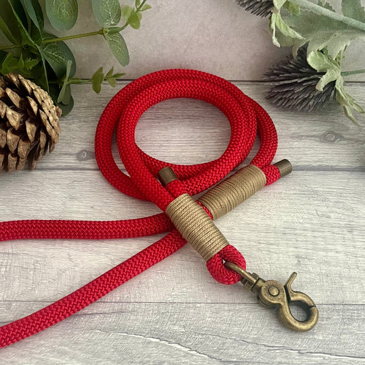 Red rope lead with Gold Brown whipping securing a swivel clip at one end and fastening a handle at the other. The handle has an O-ring attached. Each end of the rope is finished with a metal end cap. All hardware for this lead is in Antique Brass