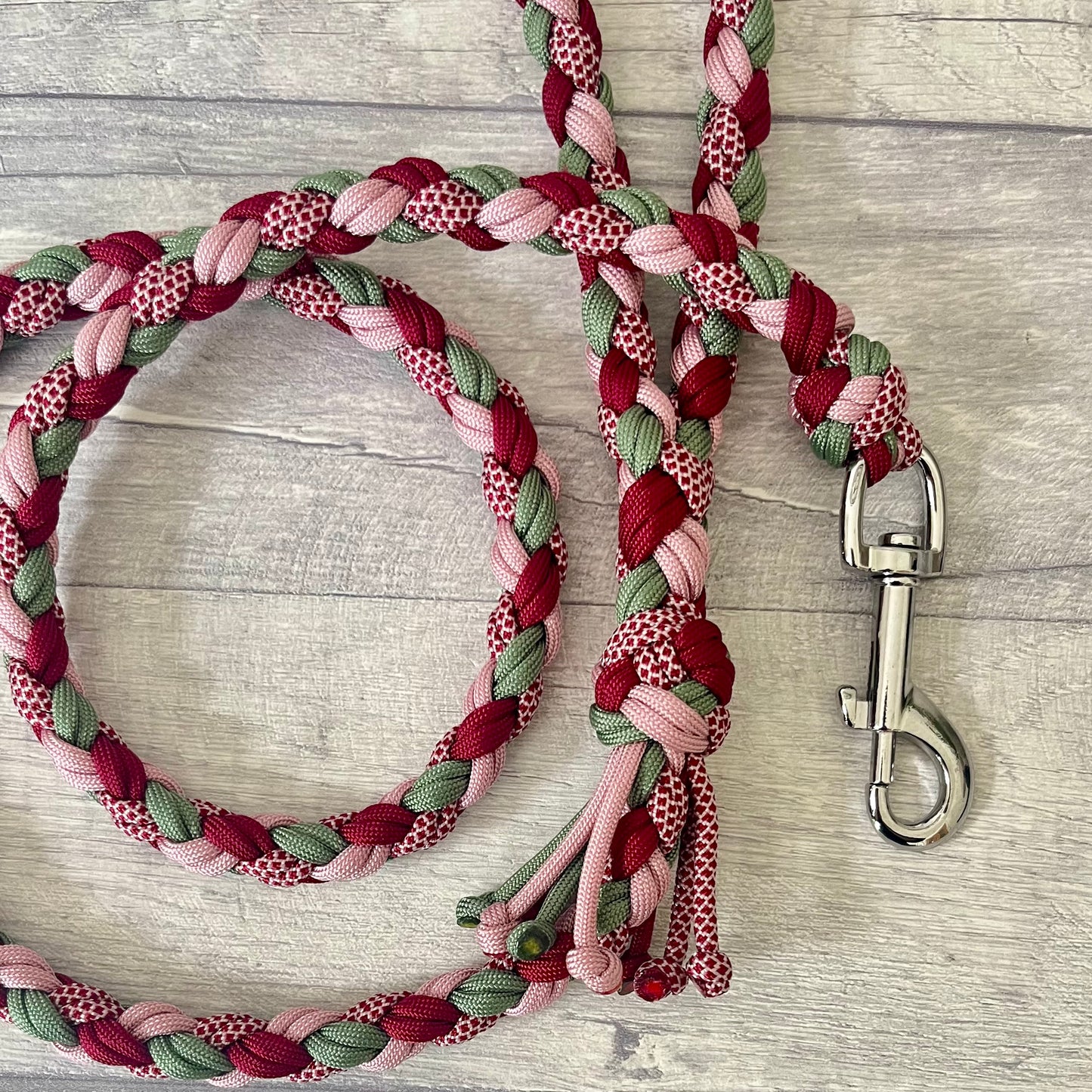 Braided dog leash with pink, green, and red pattern with a silver snap clip on a wooden surface