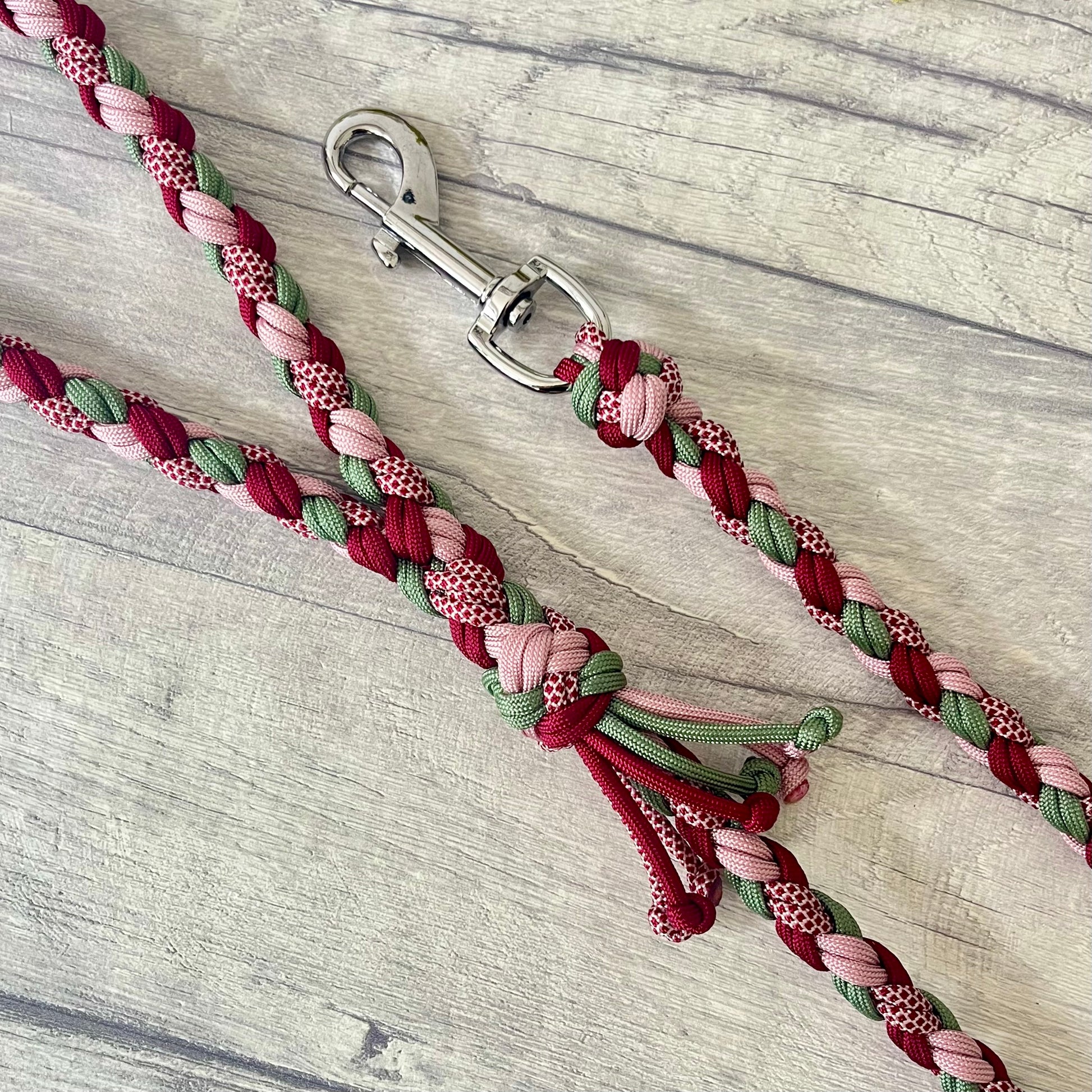 Braided dog leash with pink, green, and red pattern with a silver snap clip on a wooden surface