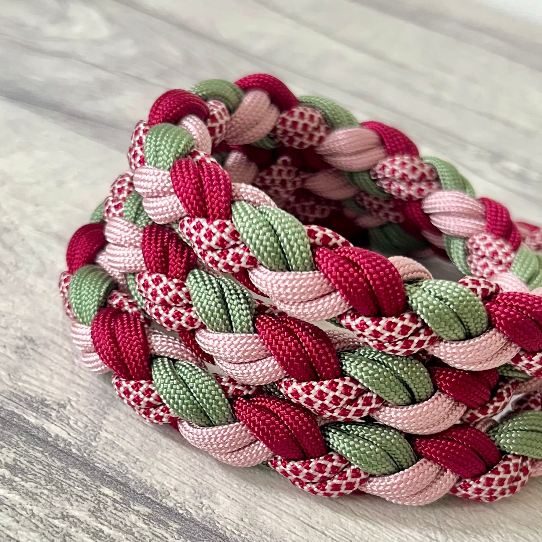Braided dog leash with pink, green, and red pattern on a wooden surface