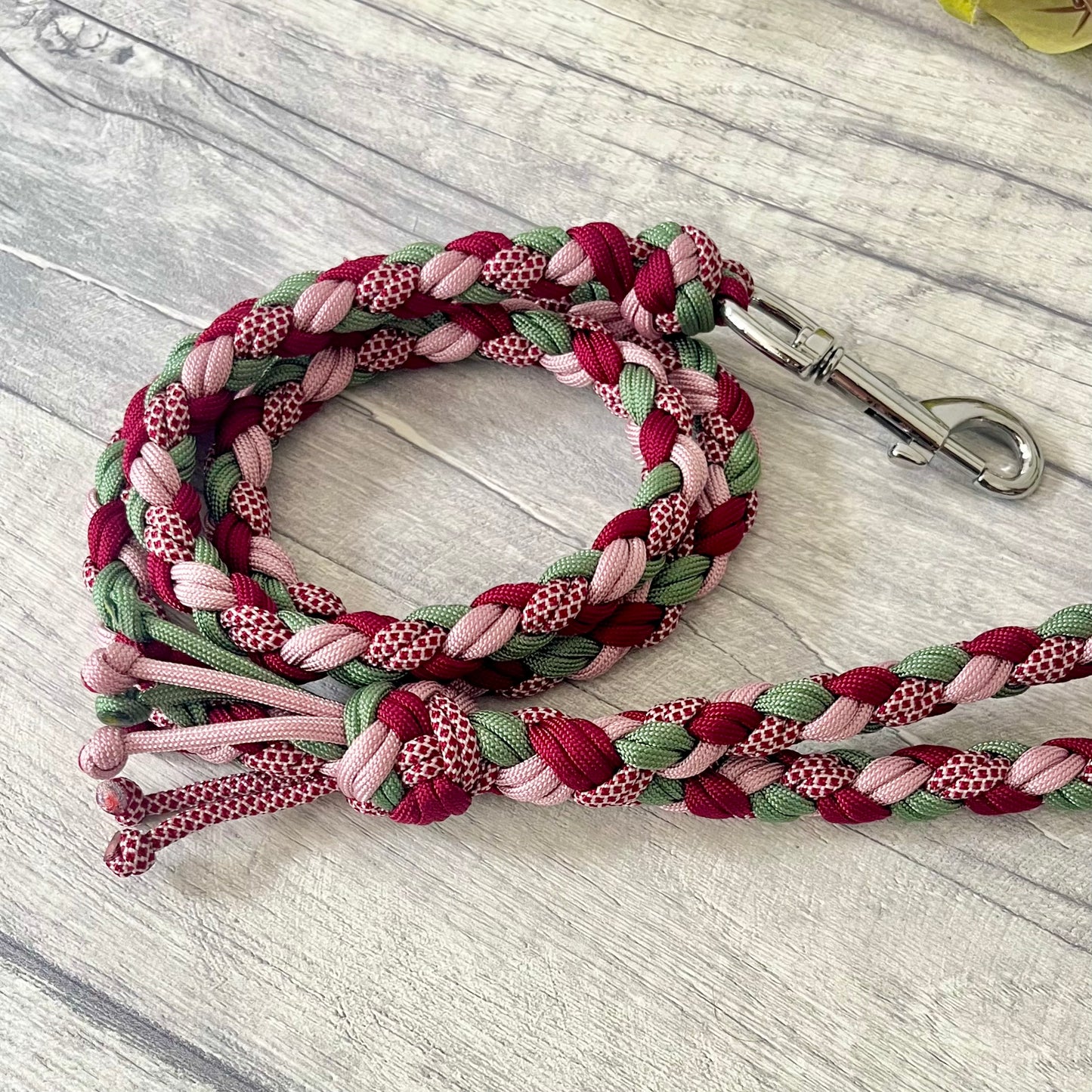 Braided dog leash with pink, green, and red pattern with a silver snap clip on a wooden surface