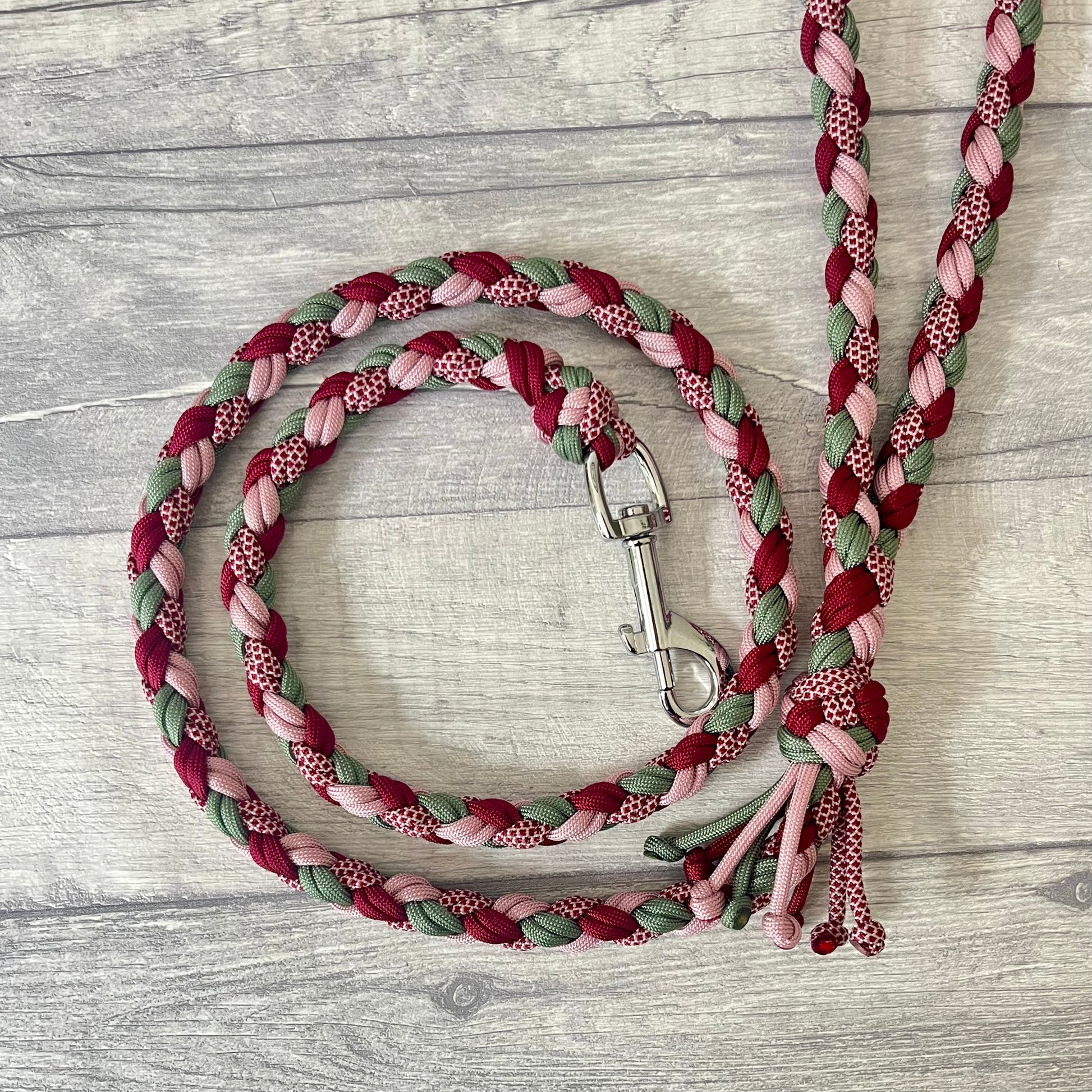 Braided dog leash with pink, green, and red pattern with a silver snap clip on a wooden surface