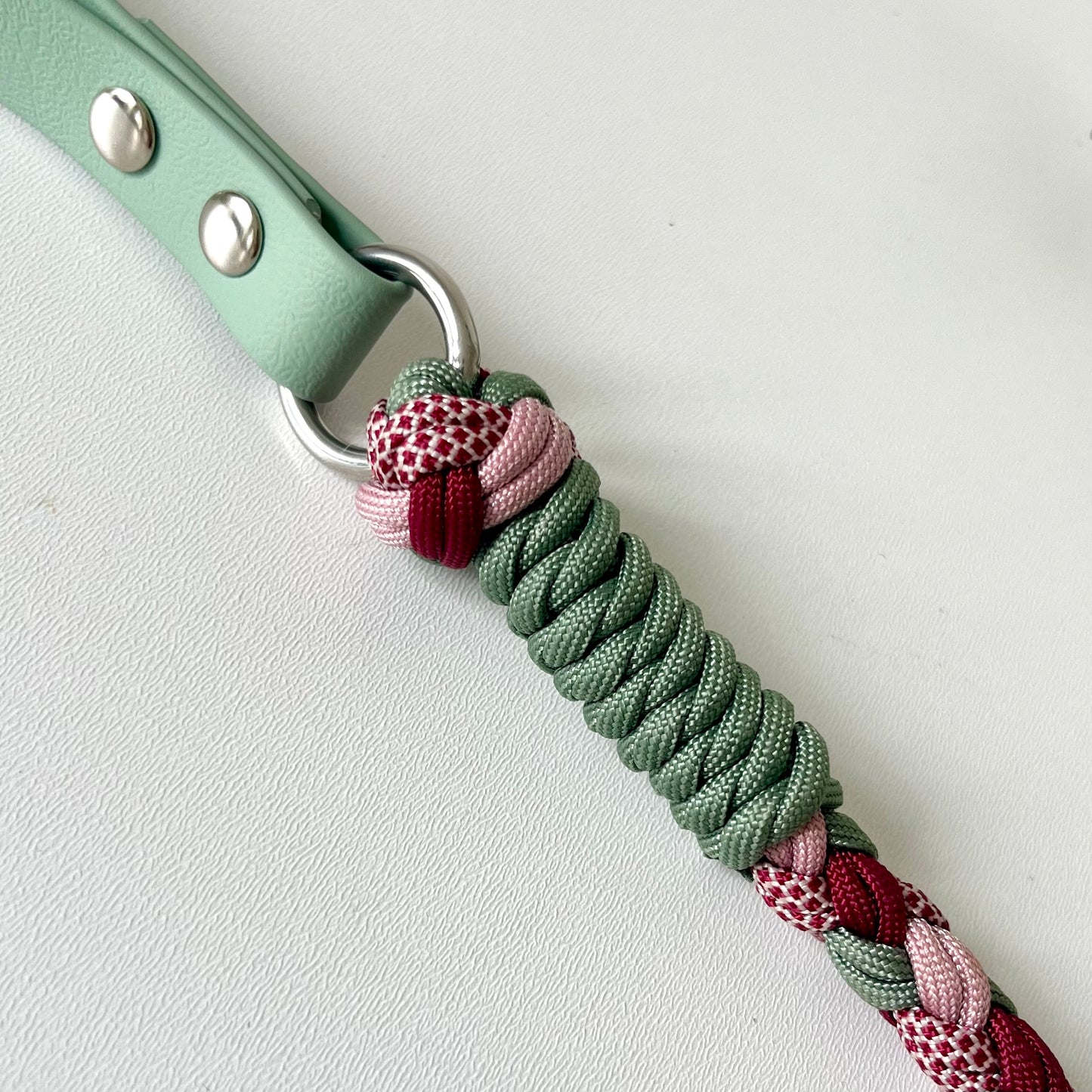 Green braided strap with a metal ring attached to a green biothane handle on a light gray background