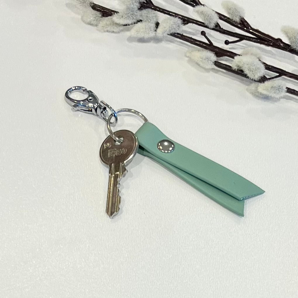 A green biothane keyring with a clip and key attached sitting on a white surface