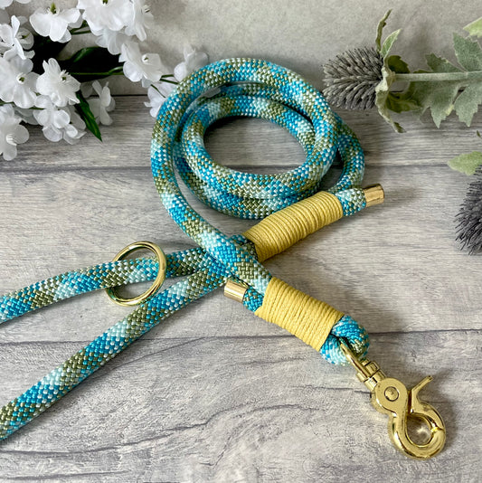 Bombay Blue rope lead with Pastel Yellow whipping securing a swivel clip at one end and fastening a handle at the other. The handle has an O-ring attached. Each end of the rope is finished with a metal end cap. All hardware for this lead is in Gold