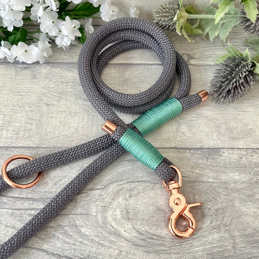 Charcoal Grey rope lead with Sea Green whipping securing a swivel clip at one end and fastening a handle at the other. The handle has an O-ring attached. Each end of the rope is finished with a metal end cap. All hardware for this lead is in Rose Gold