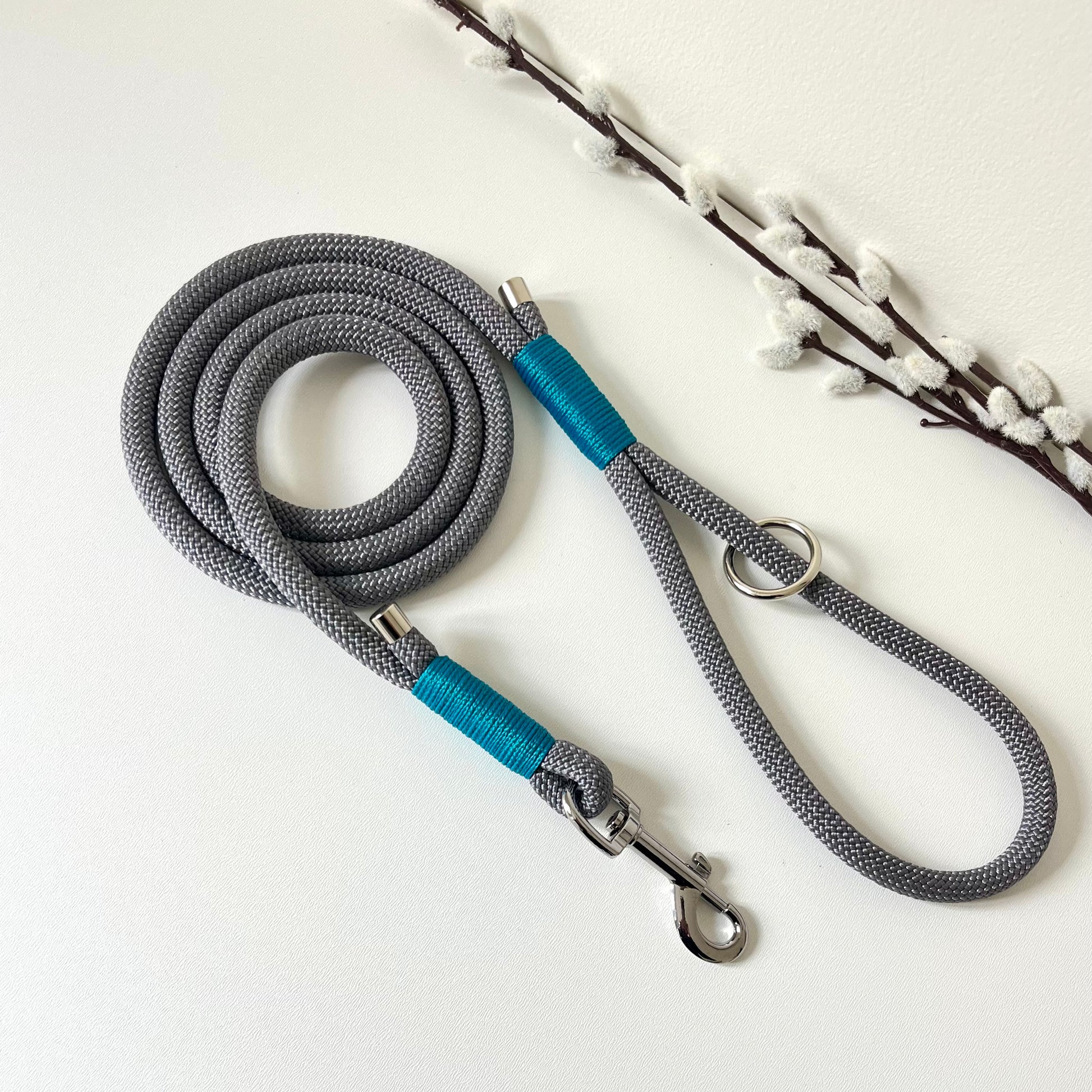 A charcoal grey rope dog lead with tan binding and silver hardware sitting on a white surface