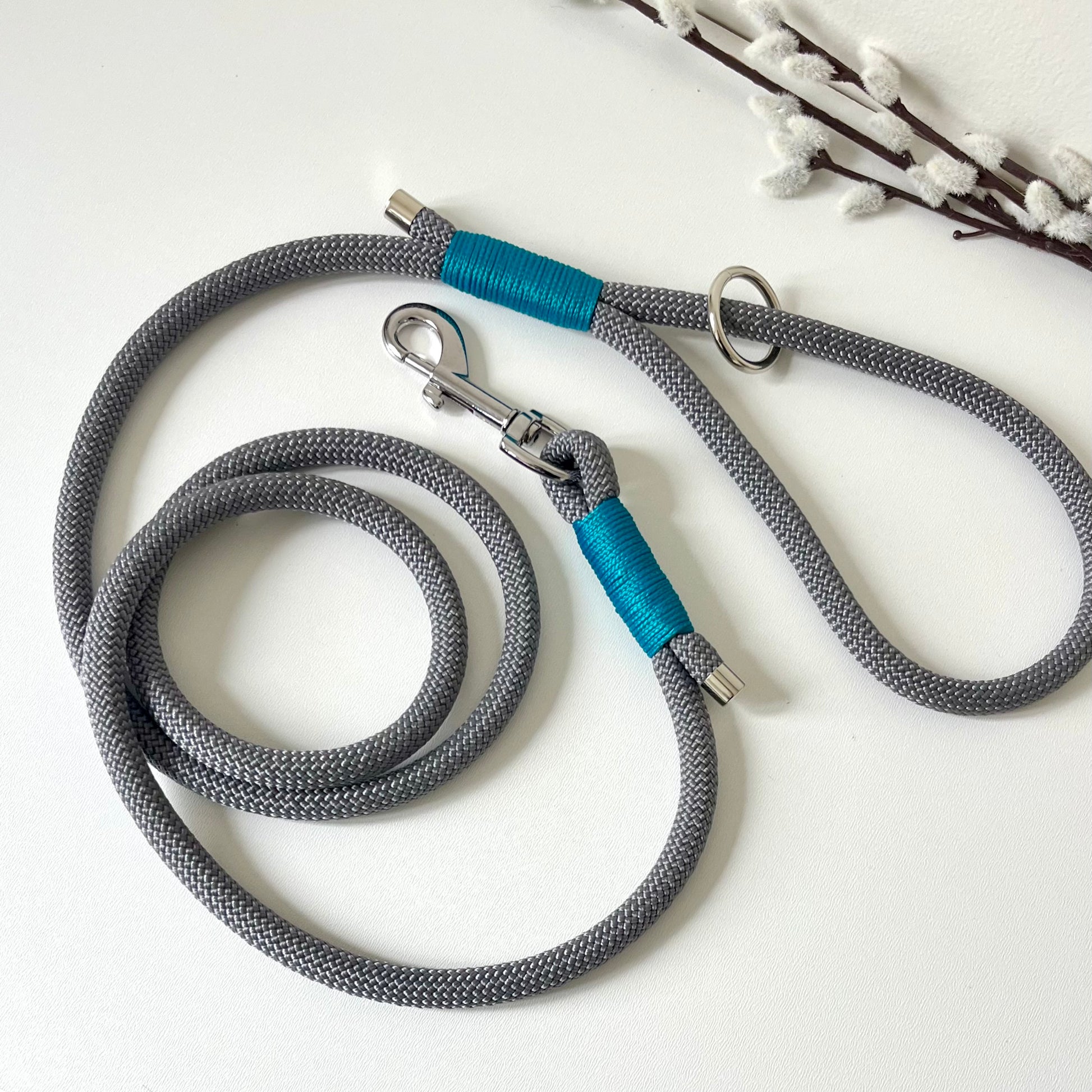 A charcoal grey rope dog lead with tan binding and silver hardware sitting on a white surface