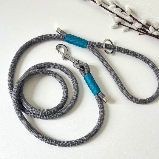A charcoal grey rope dog lead with tan binding and silver hardware sitting on a white surface