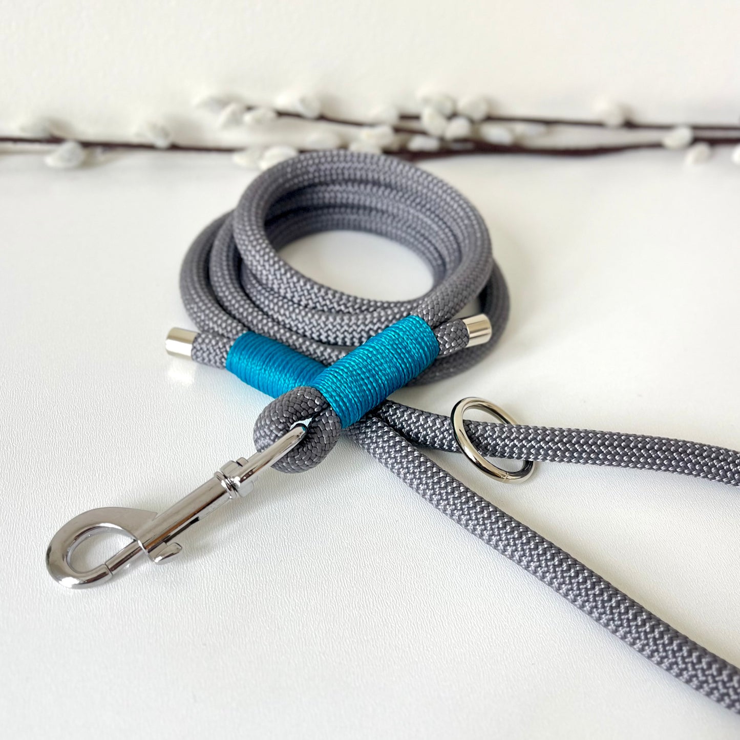 A charcoal grey rope dog lead with tan binding and silver hardware sitting on a white surface