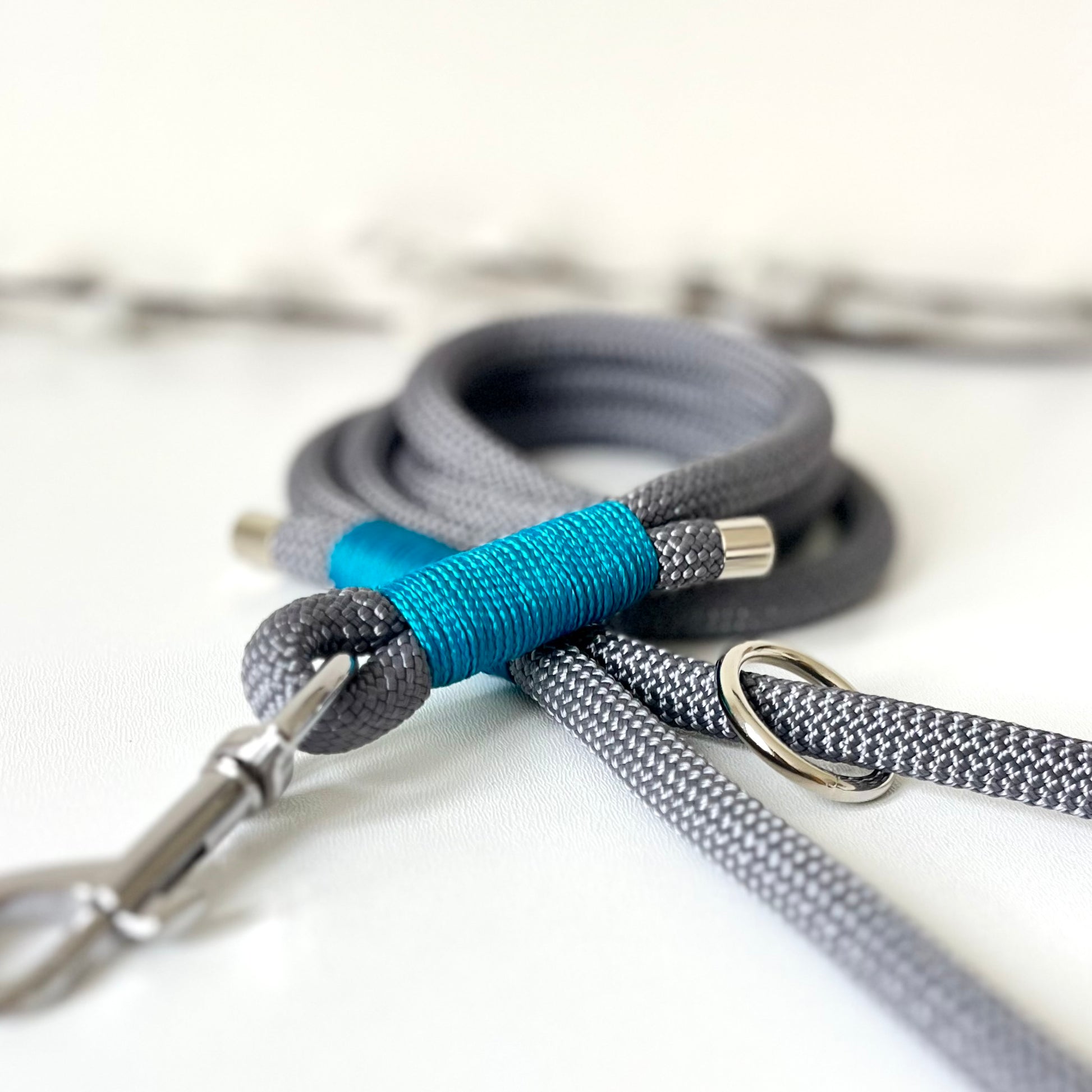 A charcoal grey rope dog lead with tan binding and silver hardware sitting on a white surface