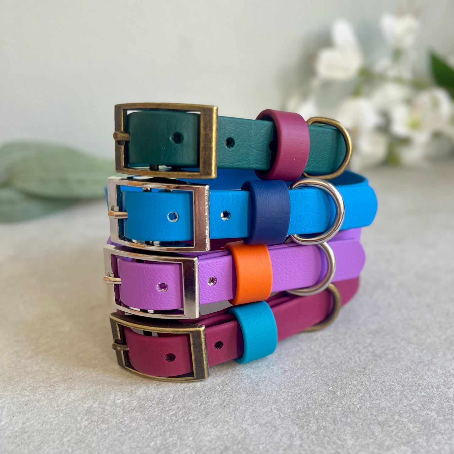Stack of colorful dog collars with metal buckles on a light surface.