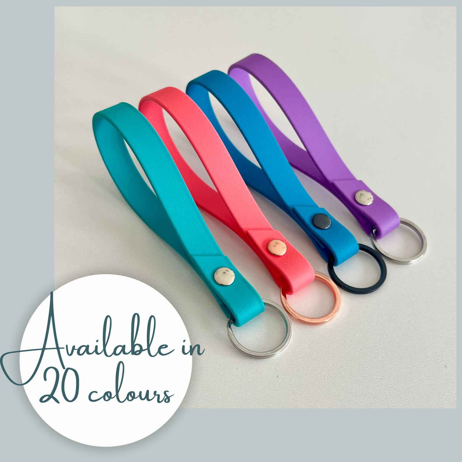 four colourful biothane key rings with text indicating  availability on a light surface