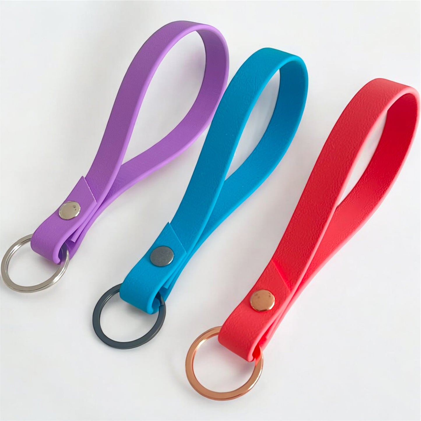 three colourful biothane key rings on a light surface