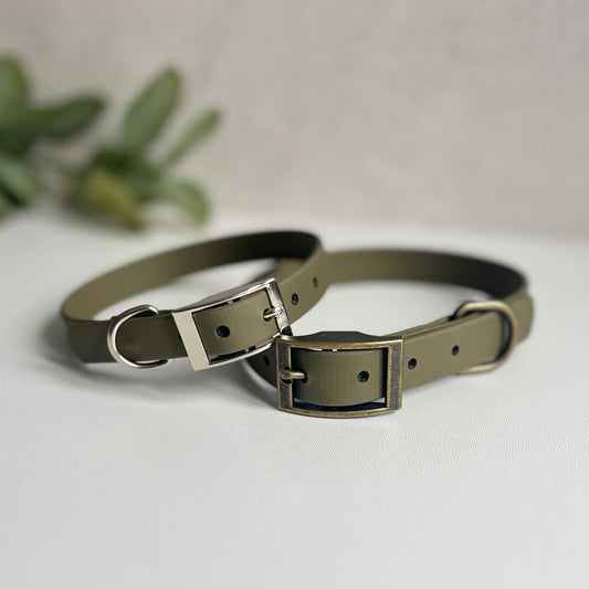 Two olive biothane dog collars with sliver and antique brass hardware sitting on a white surface