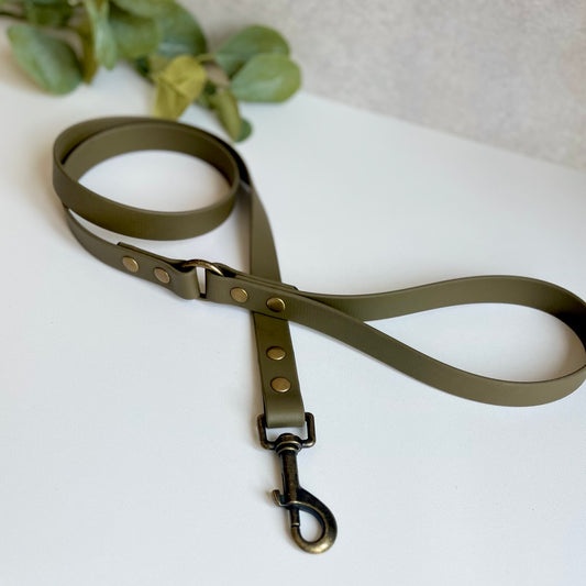 Military Olive Green Biothane lead with Antique Brass Hardware. An O-ring connects the handle to the lead with double ended rivets fixing it together. A Snap Clip is fixed with double ended rivets. The lead has a soft leather appearance.