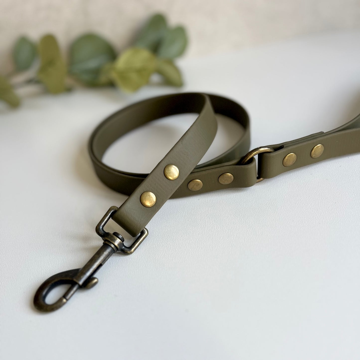 Military Olive Green Biothane lead with Antique Brass Hardware. An O-ring connects the handle to the lead with double ended rivets fixing it together. A Snap Clip is fixed with double ended rivets. The lead has a soft leather appearance.