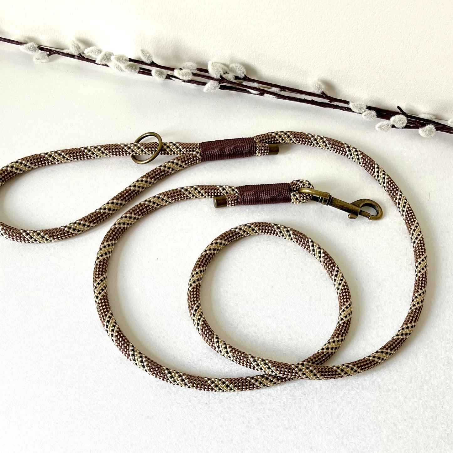 Brown rope dog lead with binding and antique brass hardware on a white surface