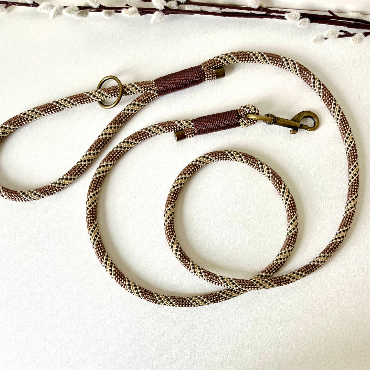 Brown rope dog lead with binding and antique brass hardware on a white surface