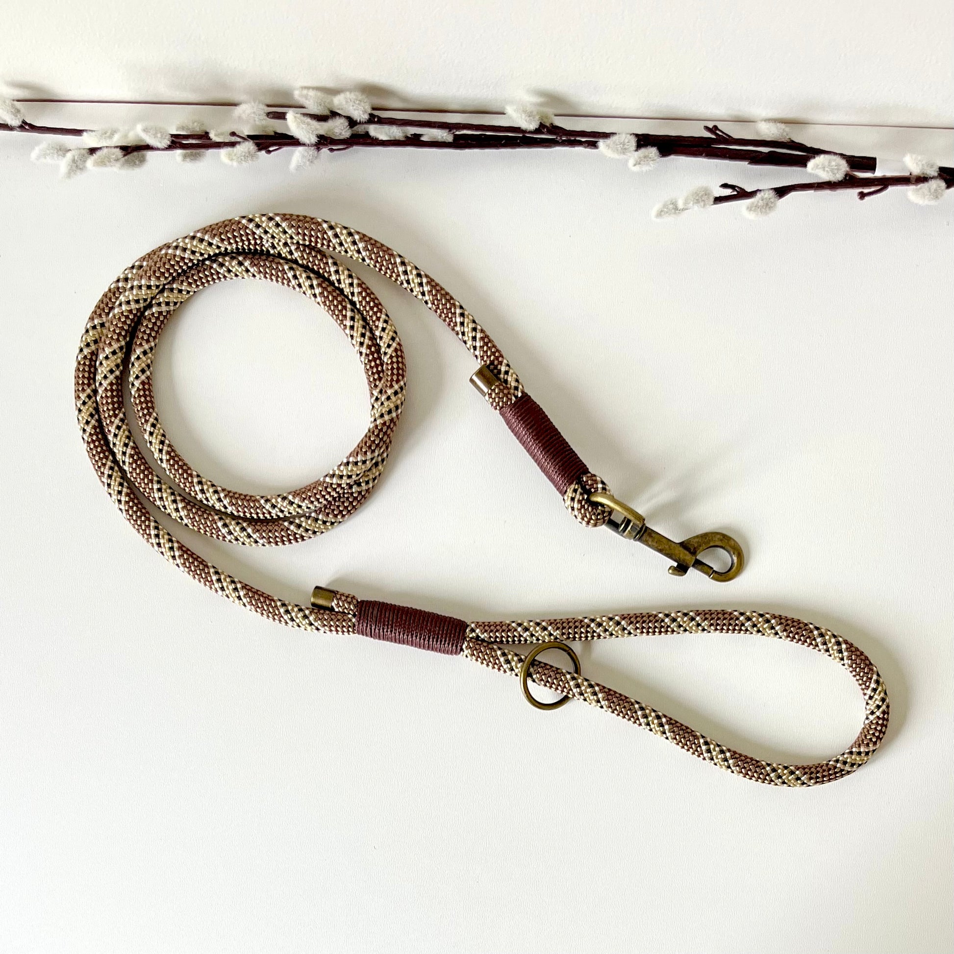 Brown rope dog lead with binding and antique brass hardware on a white surface