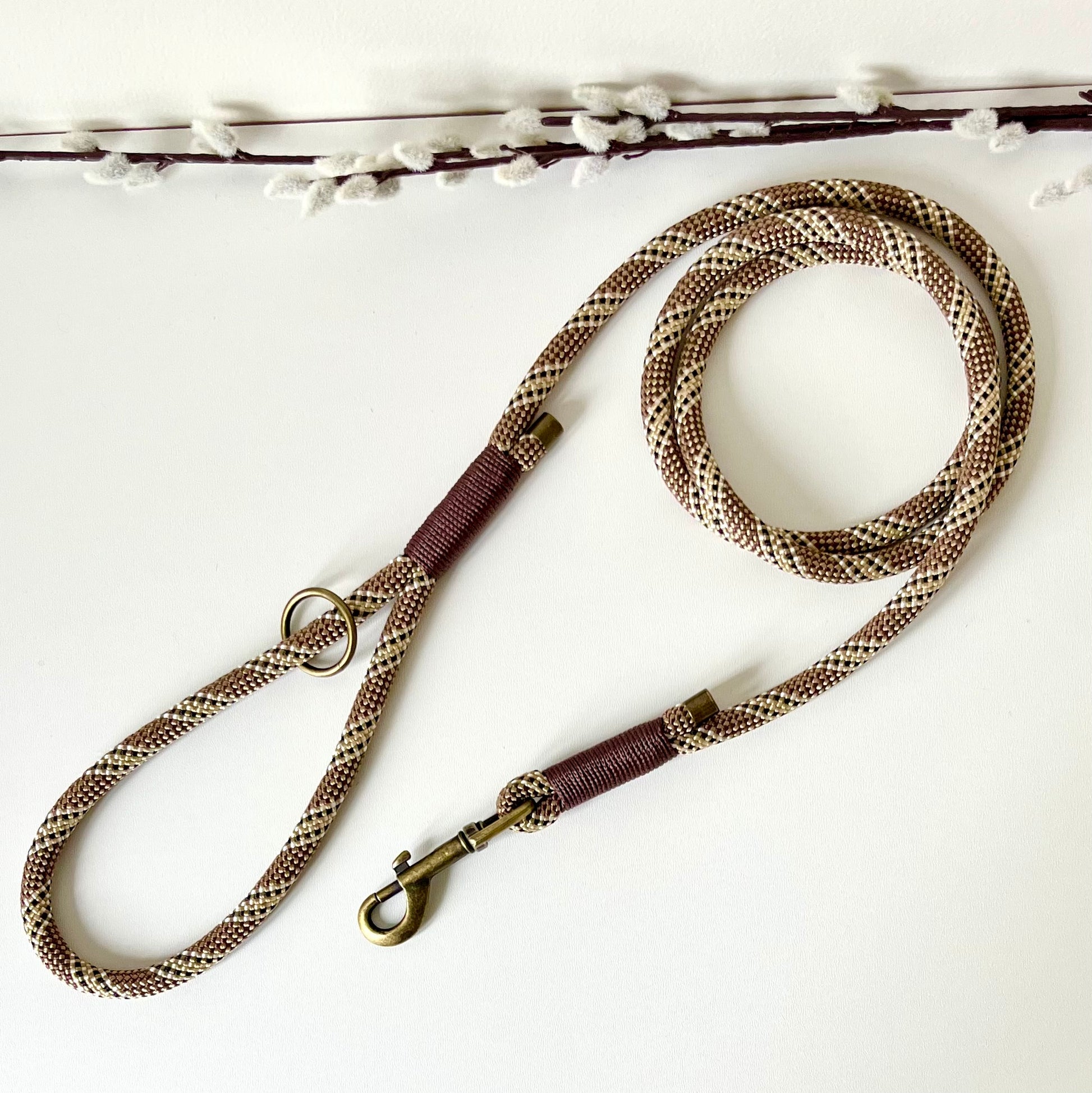 Brown rope dog lead with binding and antique brass hardware on a white surface