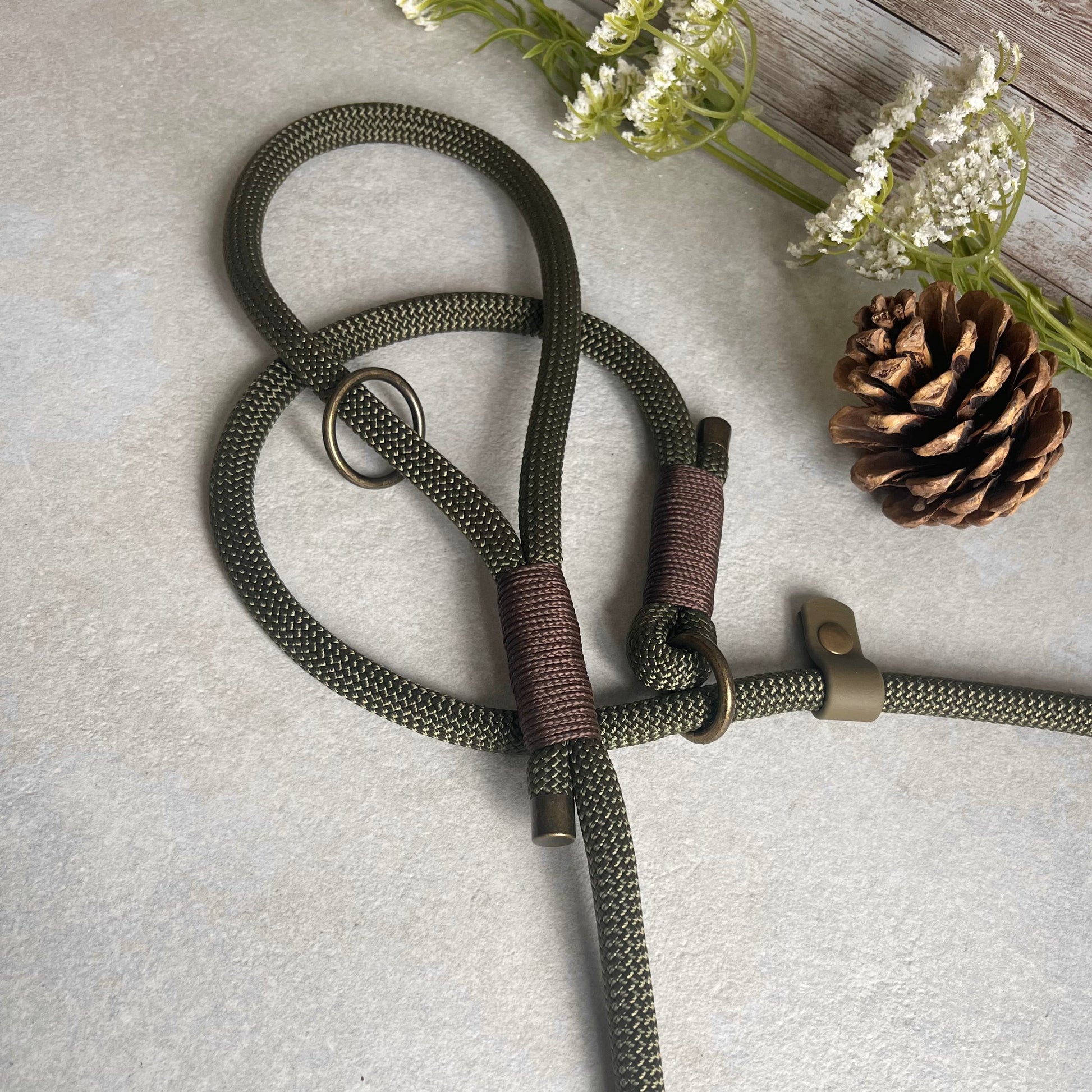 Olive Green Paracord rope slip lead with Brown whipping securing each end together. At each end of the rope there is a metal end cap with a Biothane stopper and a O-ring fixed to the handle. All hardware is Antique Brass