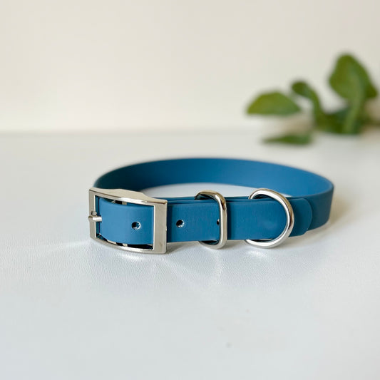A blue Biothane dog collar with silver hardware sitting on a white surface
