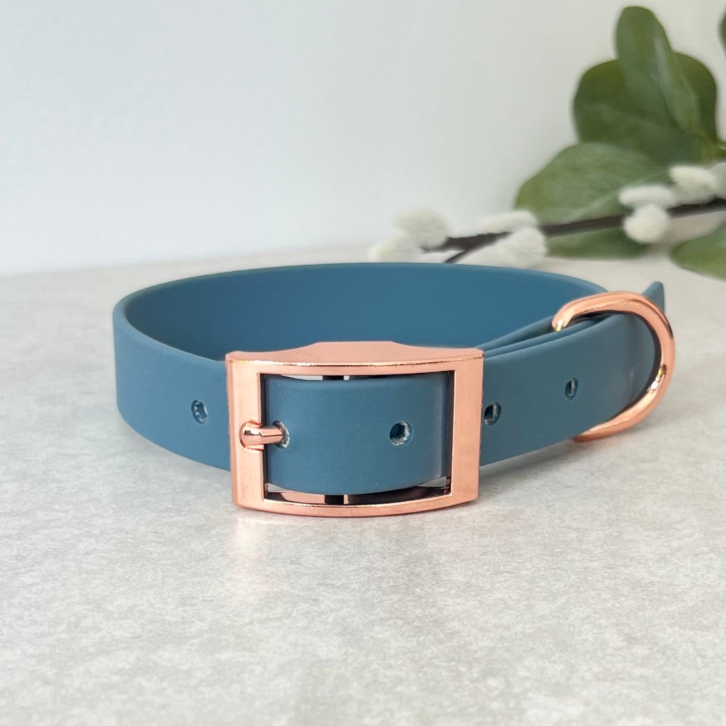 Petrol Blue Biothane dog collar with Rose Gold hardware. The collar is fastened with a buckle and has a d-ring. There are 5 punched holes spaced 2cm apart.