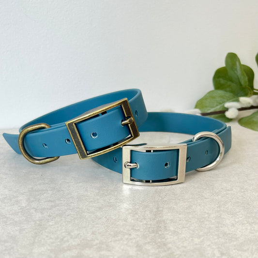 Two Petrol Blue Biothane dog collars with Antique Brass & Silver hardware. The collars are fastened with a buckle and have a d-ring. There are 5 punched holes spaced 2cm apart.
