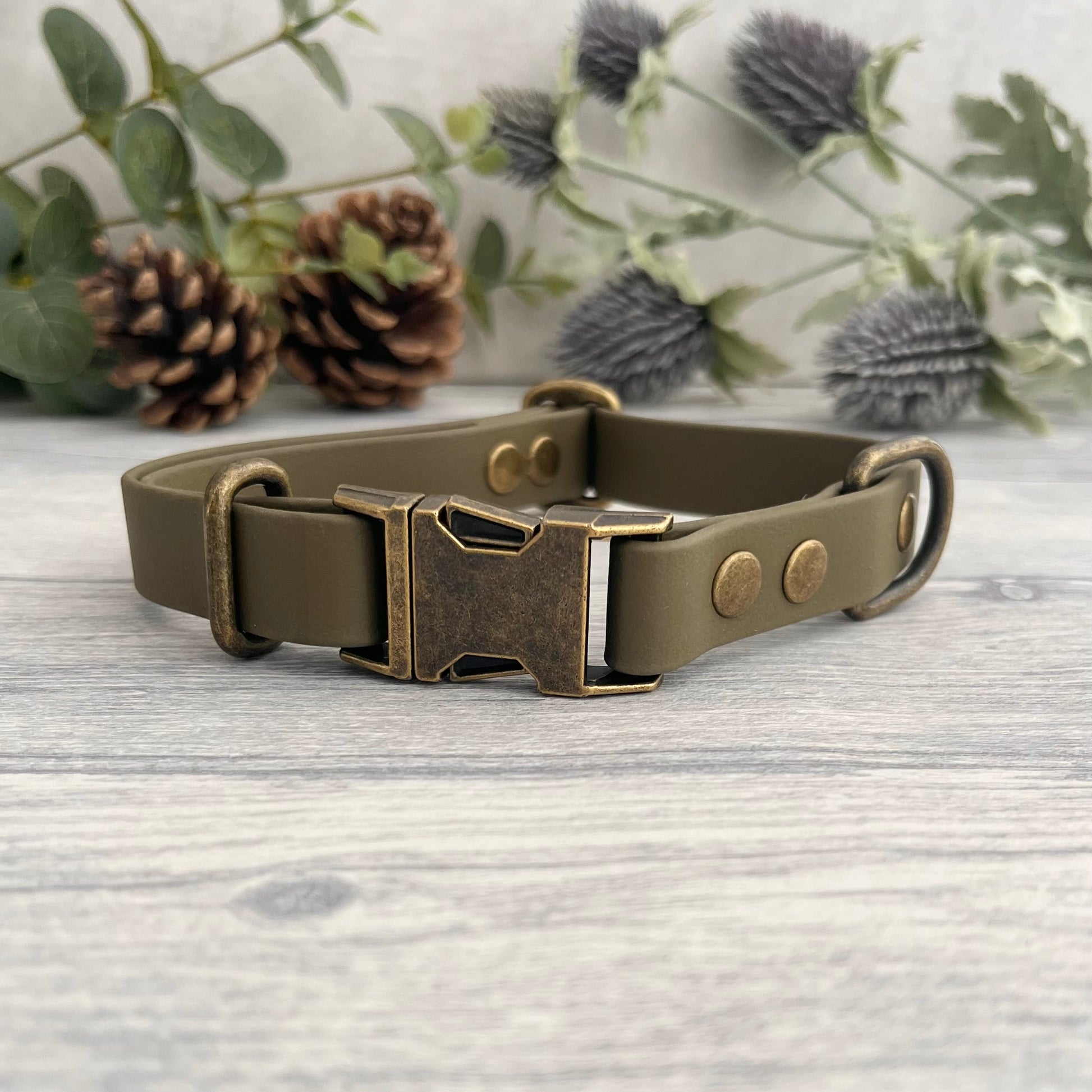 Made from Biothane in Olive Green, the collar is fastened with a metal quick release buckle, metal rivets with a metal strap keeper on one side with a D-ring on the other. All hardware is in Antique Brass