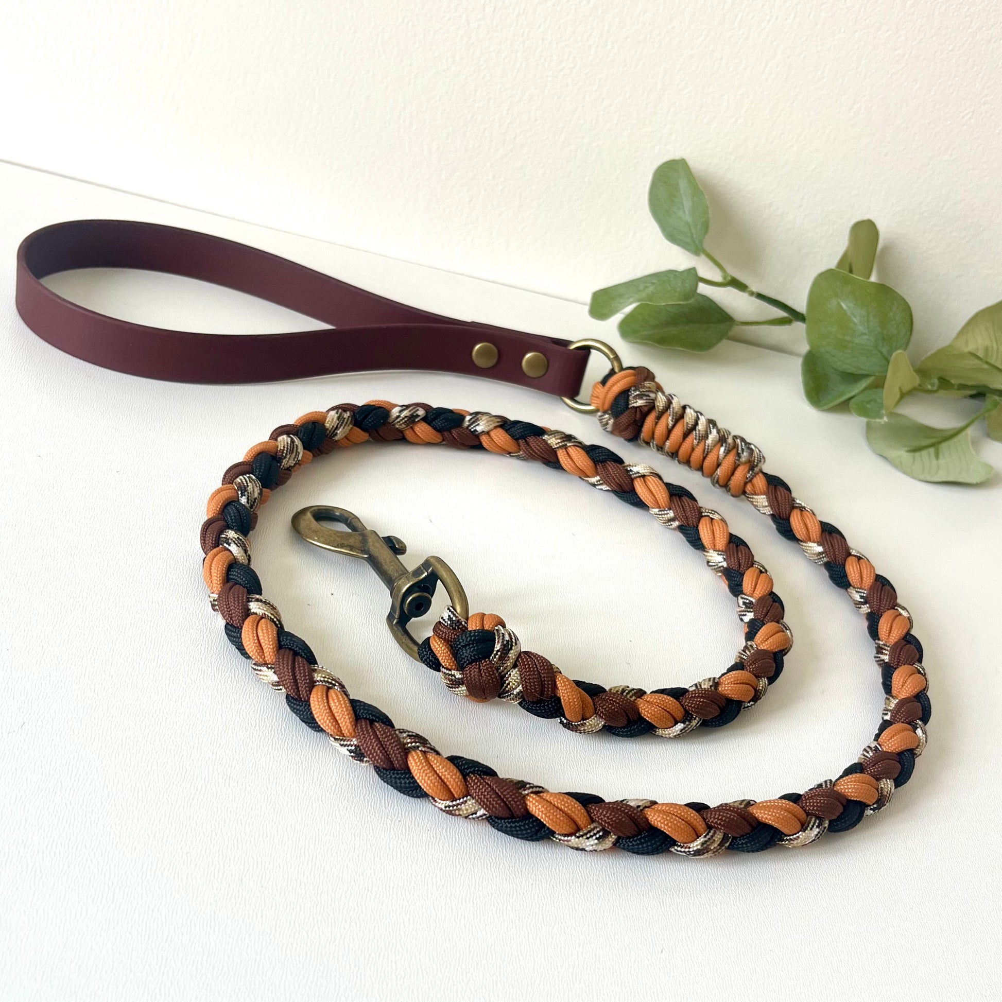Dog leash with braided design in brown, black, and orange  with a biothane handle on a white background.