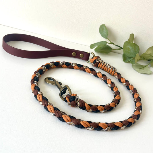 Dog leash with braided design in brown, black, and orange  with a biothane handle on a white background.