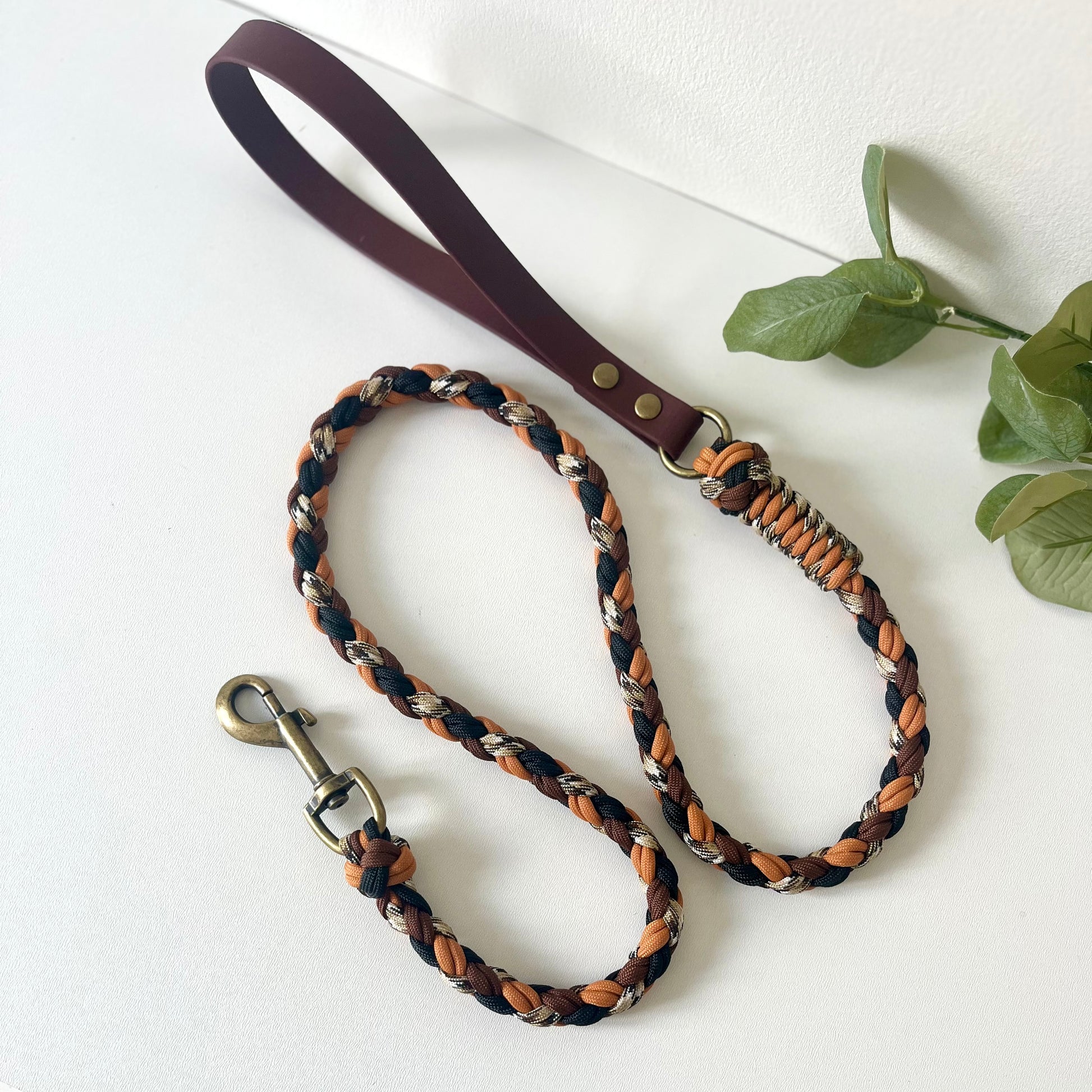 Dog leash with braided design in brown, black, and orange  with a biothane handle on a white background.
